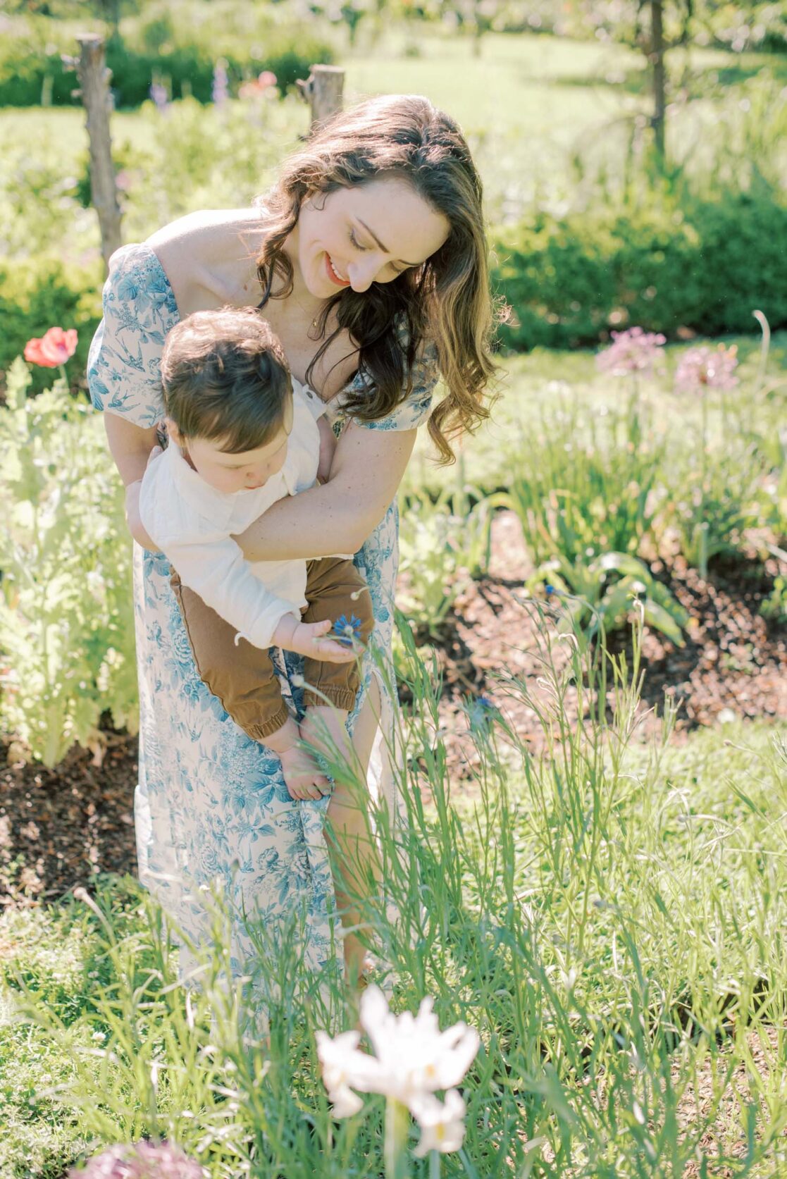 Photo of mom holding her baby son in a garden while he picks flowers by Richmond baby photographer Jacqueline Aimee Portraits