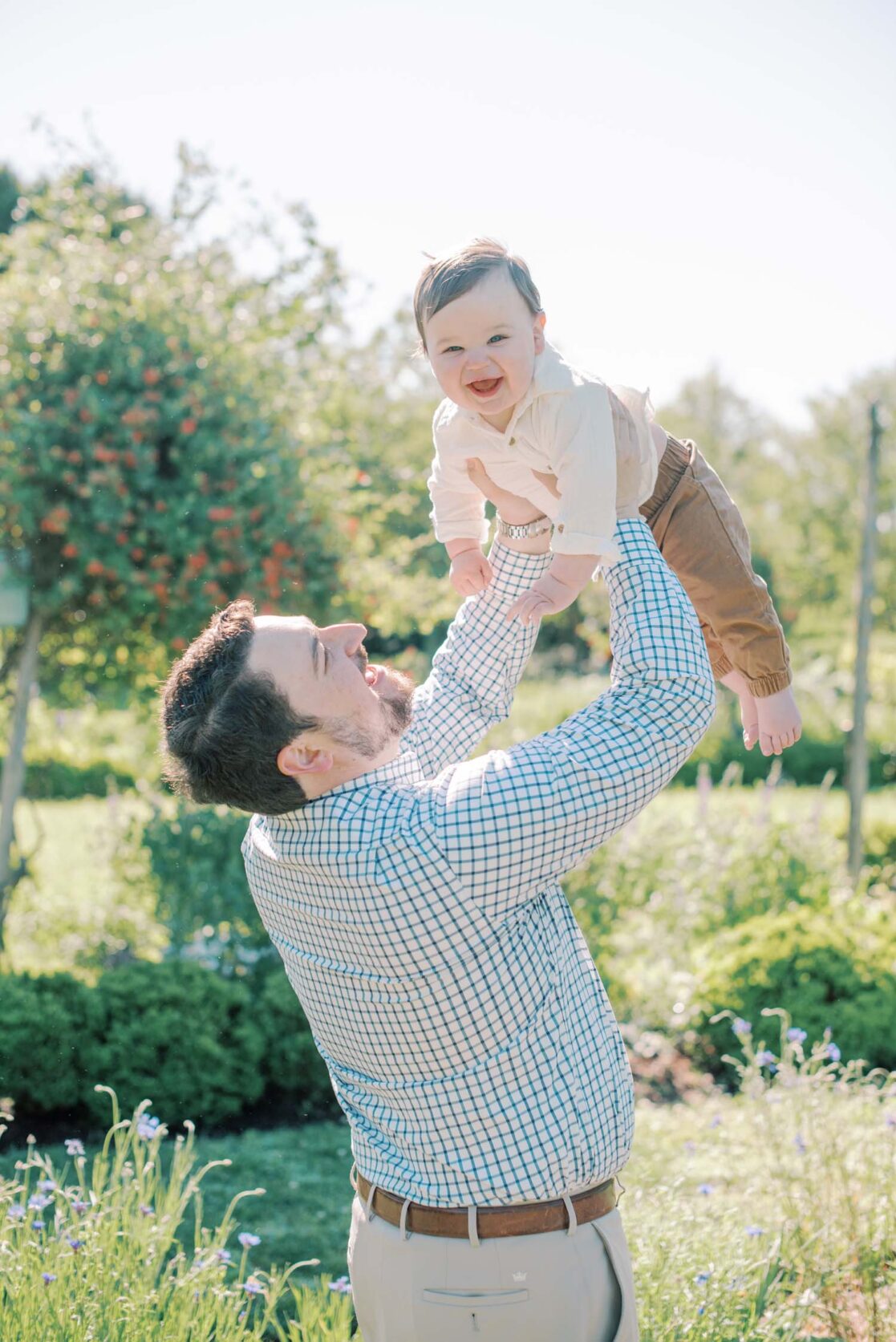 Photo of dad holding baby son up in the air in a garden Richmond baby photographer Jacqueline Aimee Portraits