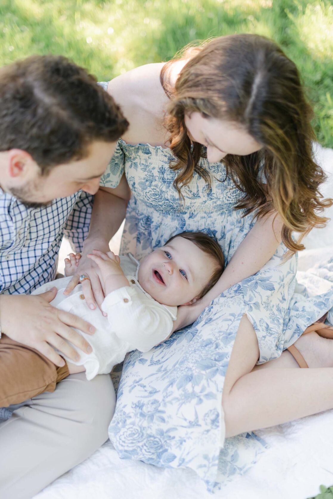 Photo of parents sitting with their one year old baby son in their laps and smiling by Richmond baby photographer Jacqueline Aimee Portraits