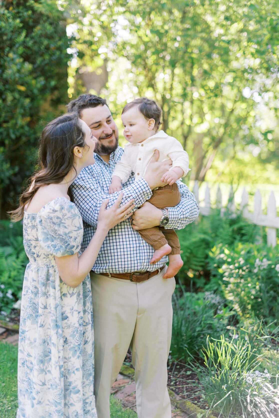 Mom and dad smiling as they hold their one year old son in a garden by Richmond baby photographer Jacqueline Aimee Portraits