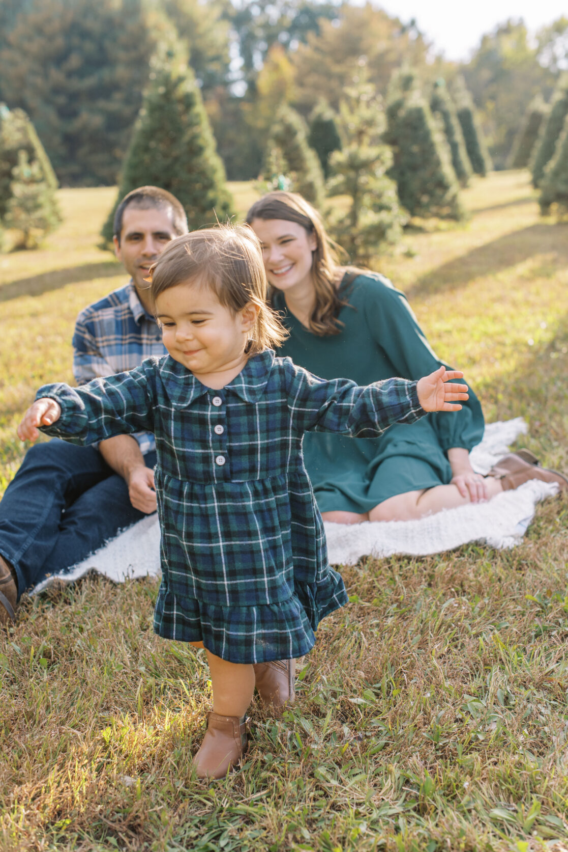 parents posed with daughter at christmas tree farm on blanket for christmas card