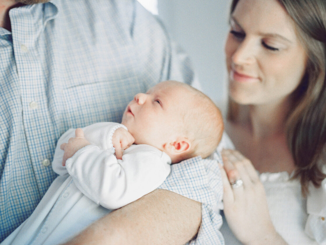 Photo of a Mom and dad holding sleepy baby in a bright Manakin Sabot newborn photo