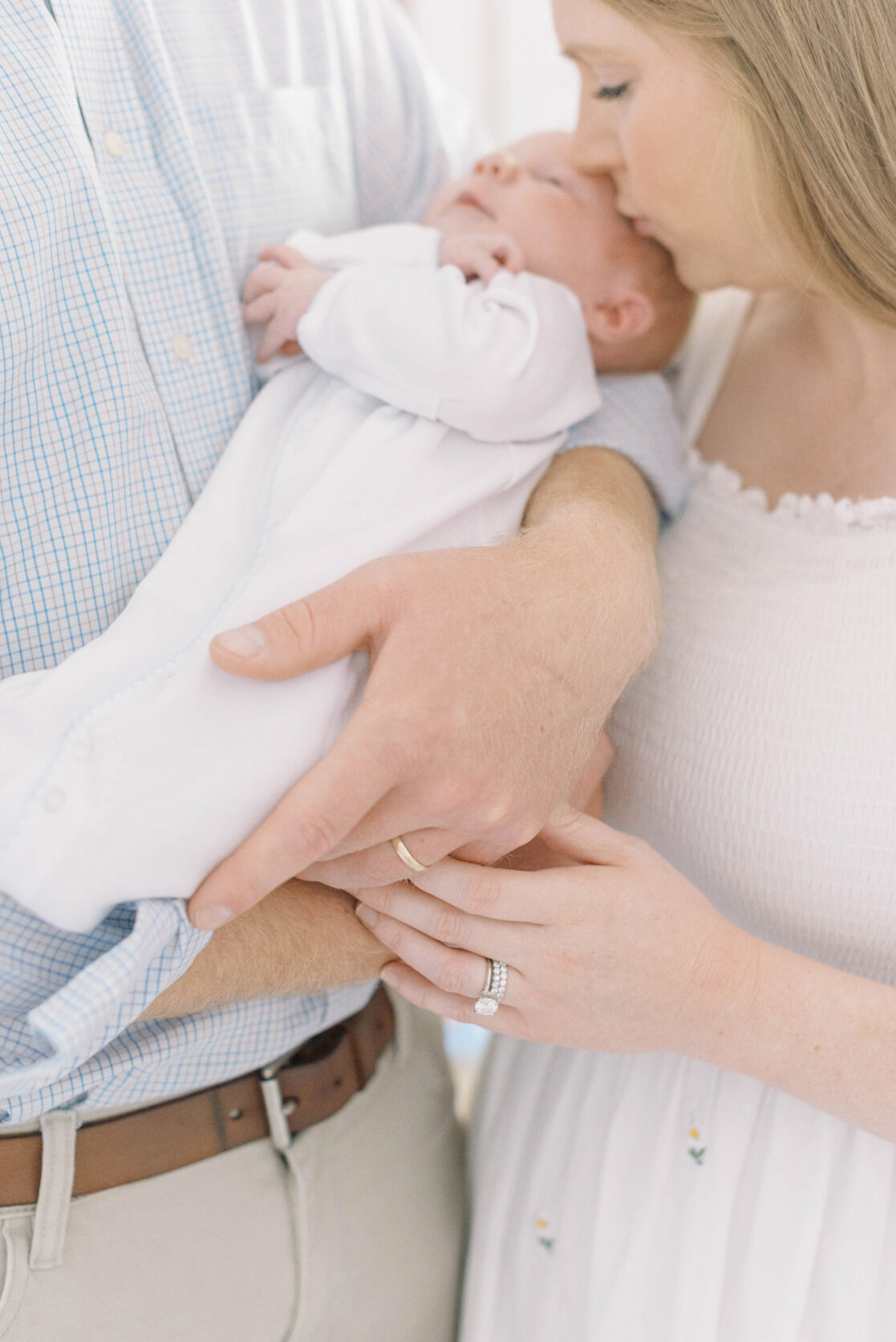 Key poses for newborn photos | Light and airy photo of a mother gently kissing her newborn baby boy on the head in his father's arms by Richmond newborn photographer Jacqueline Aimee Portraits