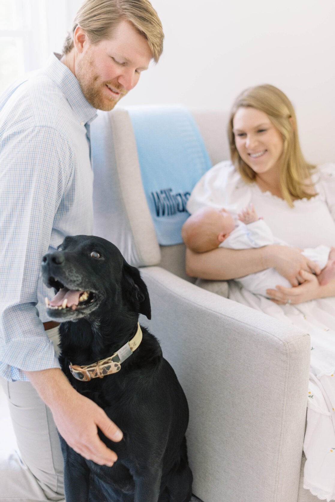 Key poses for newborn photos | Light and airy photo of a mother and father looking down lovingly at their family black lab dog as they hold their newborn baby son by Richmond newborn photographer Jacqueline Aimee Portraits