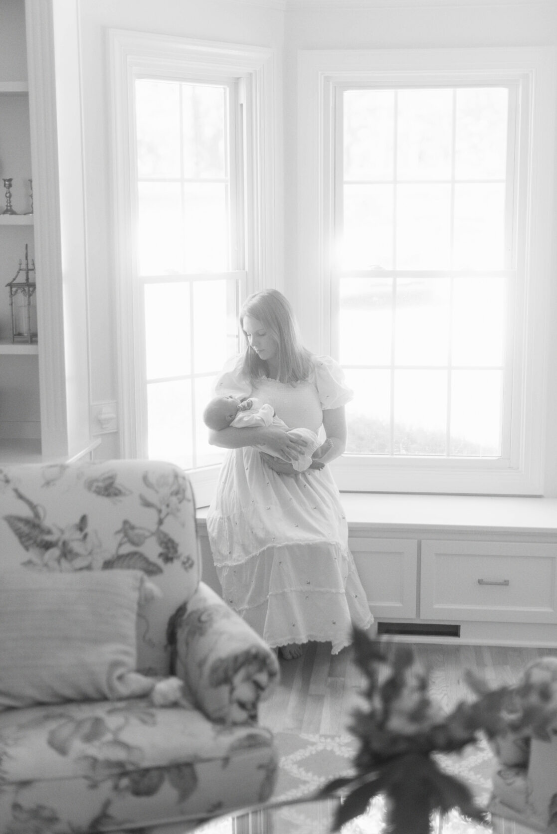 Key poses for newborn photos | Black and white photo of a mother holding her sleeping newborn baby as she sits in a bright window seat by Richmond newborn photographer Jacqueline Aimee Portraits