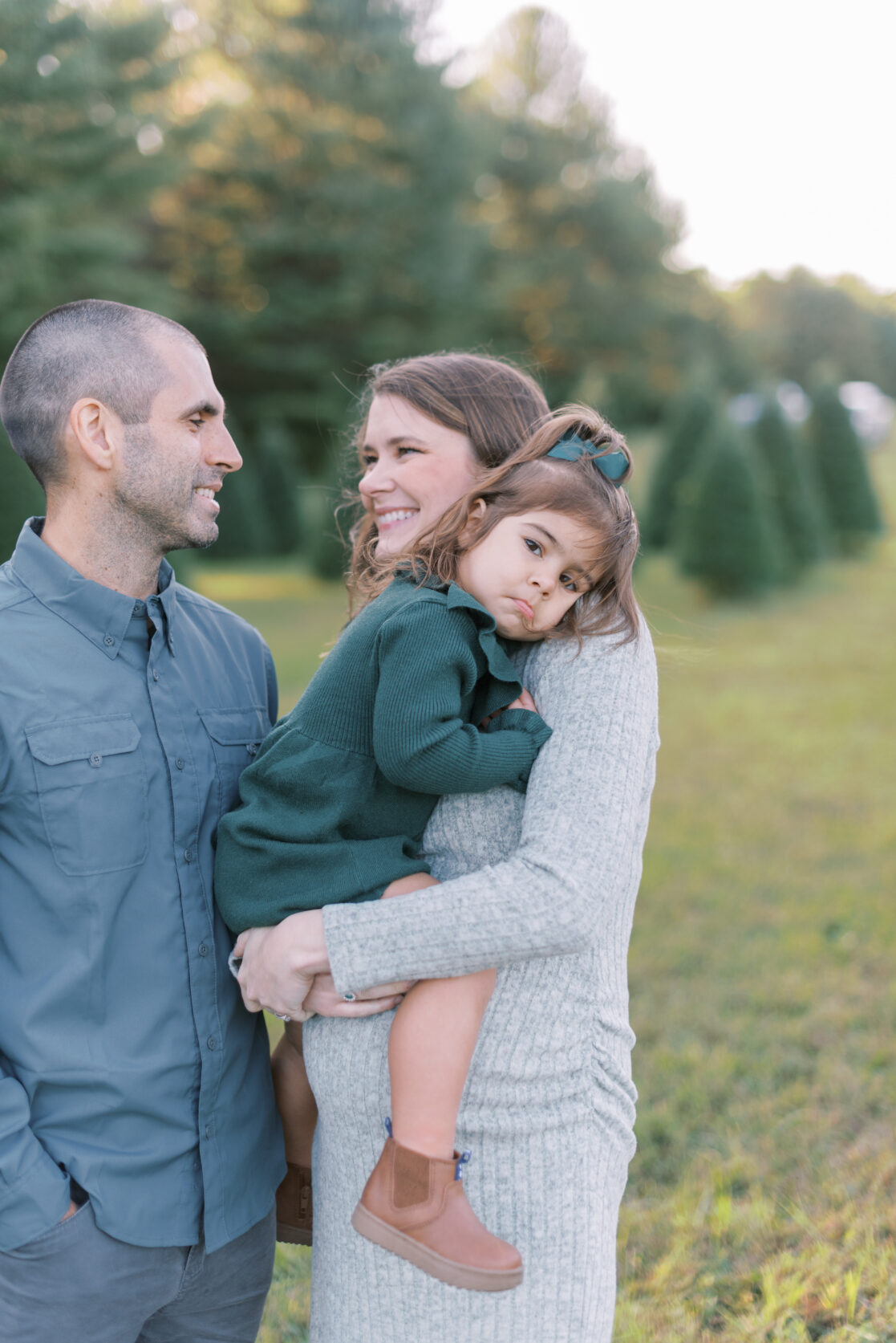 Photo of a family of three surrounded by uncut Christmas trees during their richmond fall mini session with jacqueline aimee portraits