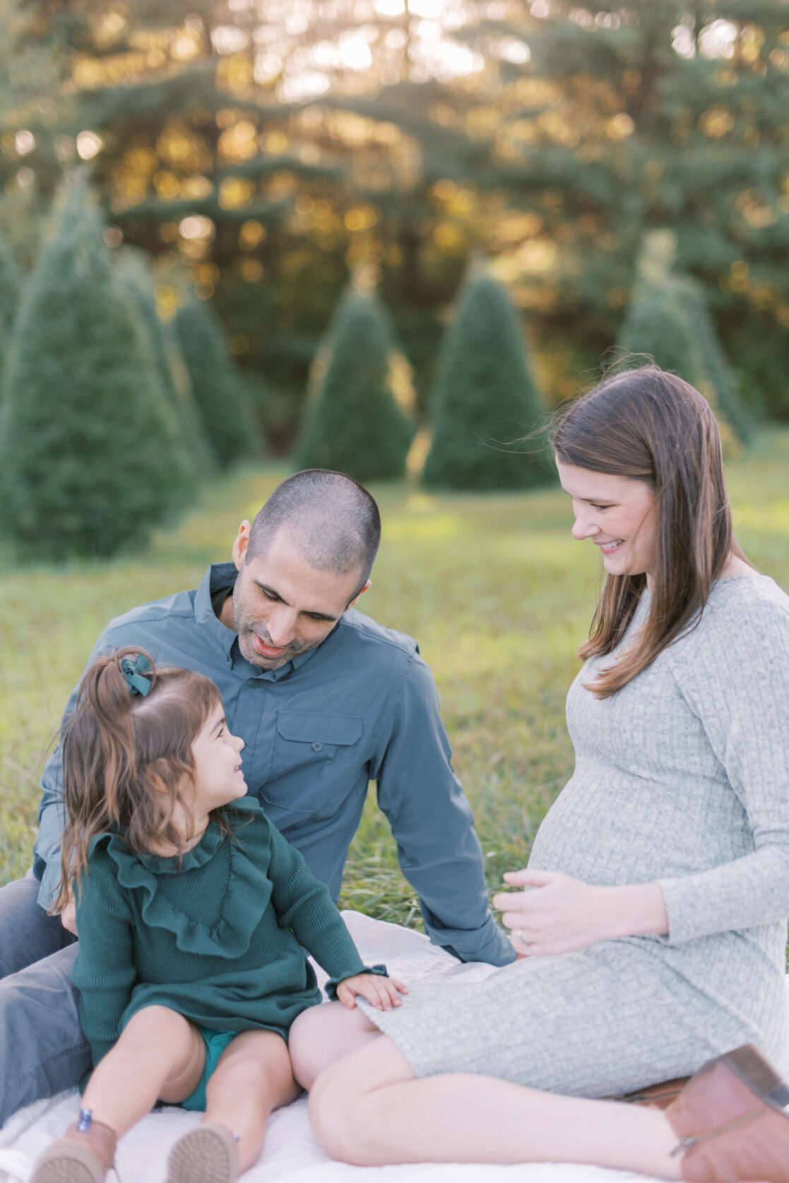 Photo of a family of three surrounded by uncut Christmas trees during their richmond fall mini session with jacqueline aimee portraits