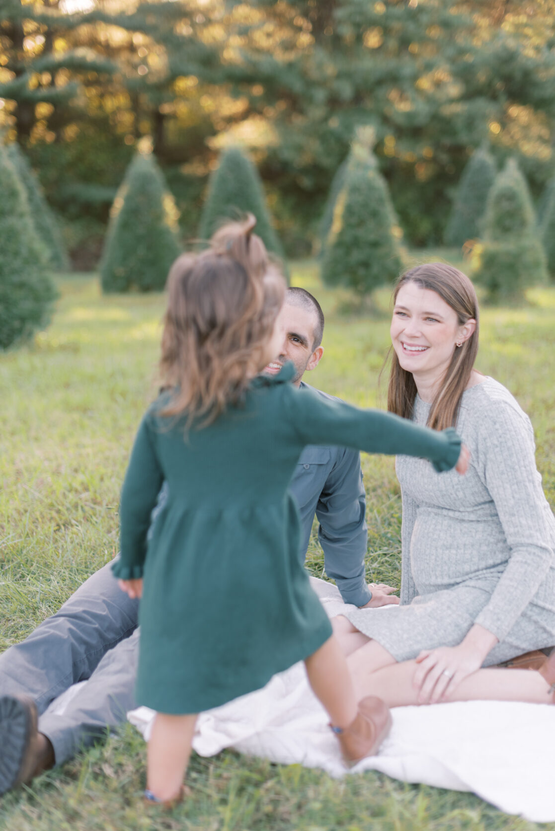 Photo of a toddler girl running to her parents surrounded by uncut Christmas trees during their richmond fall mini session with jacqueline aimee portraits