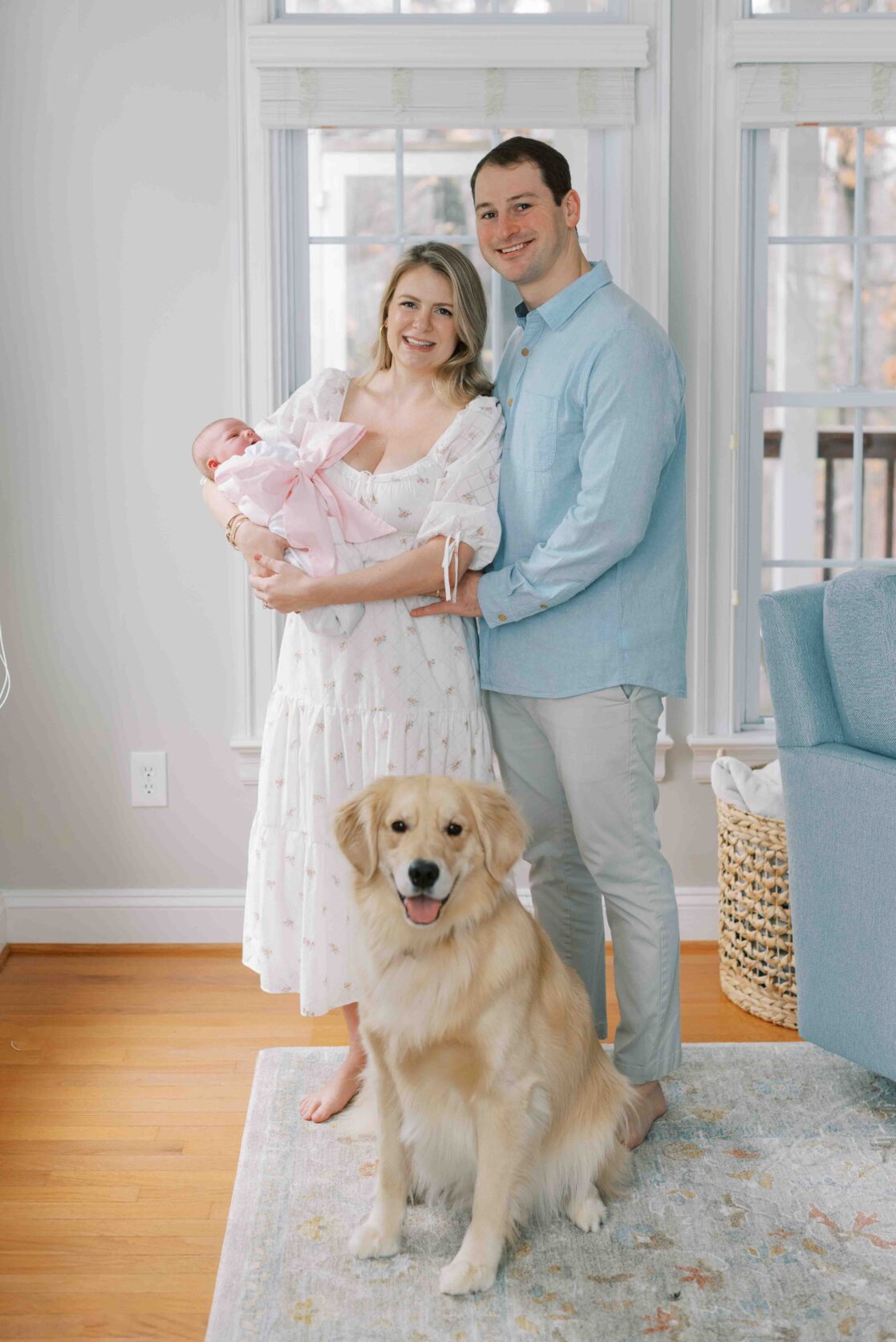 Photo of a two parents, a mom and a dad, holding their newborn daughter wrapped in a white blanket and pink bow. The parents booked their newborn photos at 10 days old, a great time if you're wondering when to schedule newborn photos 