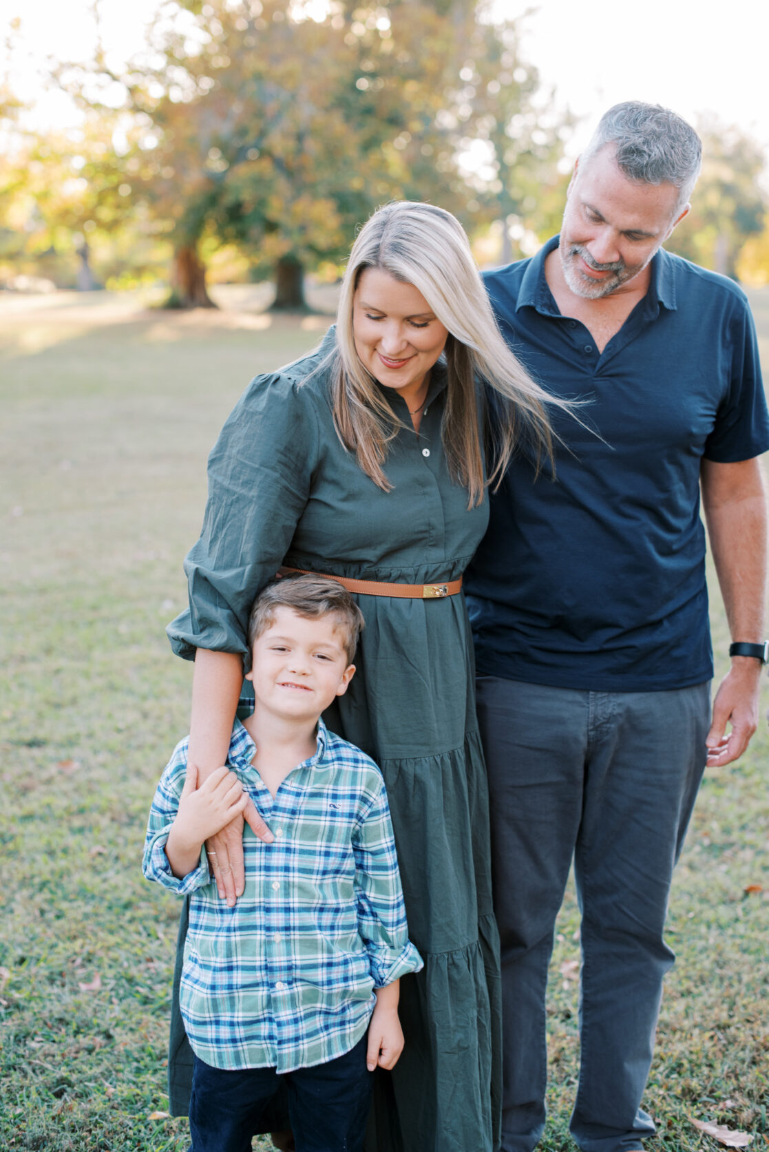 Richmond VA Fall Family Photos | Parents look at their young son in a park, surrounded by golden autumn leaves 