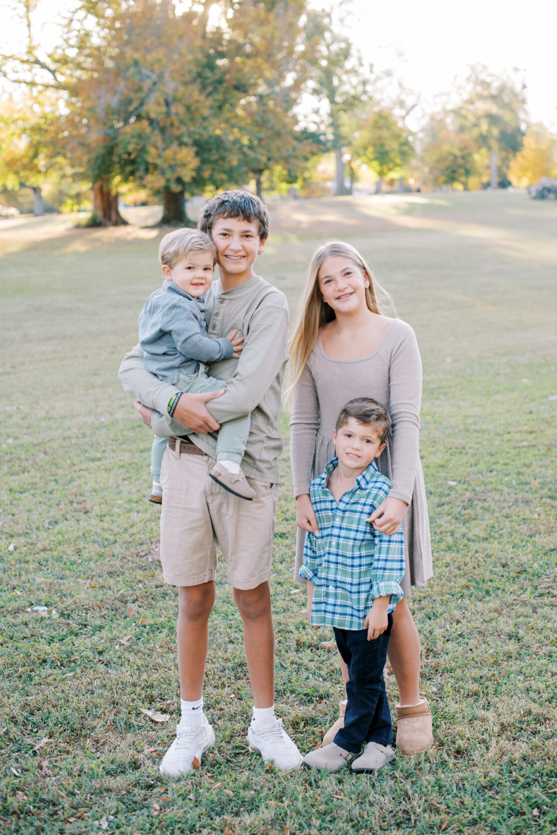 Richmond VA Fall Family Photos | Children siblings stand together for a photo in a park, surrounded by golden autumn leaves at sunset