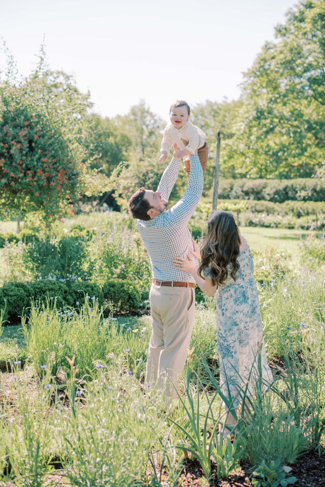Photo of dad holding baby son up in the air in a garden while mom looks on and smiles Richmond baby photographer Jacqueline Aimee Portraits