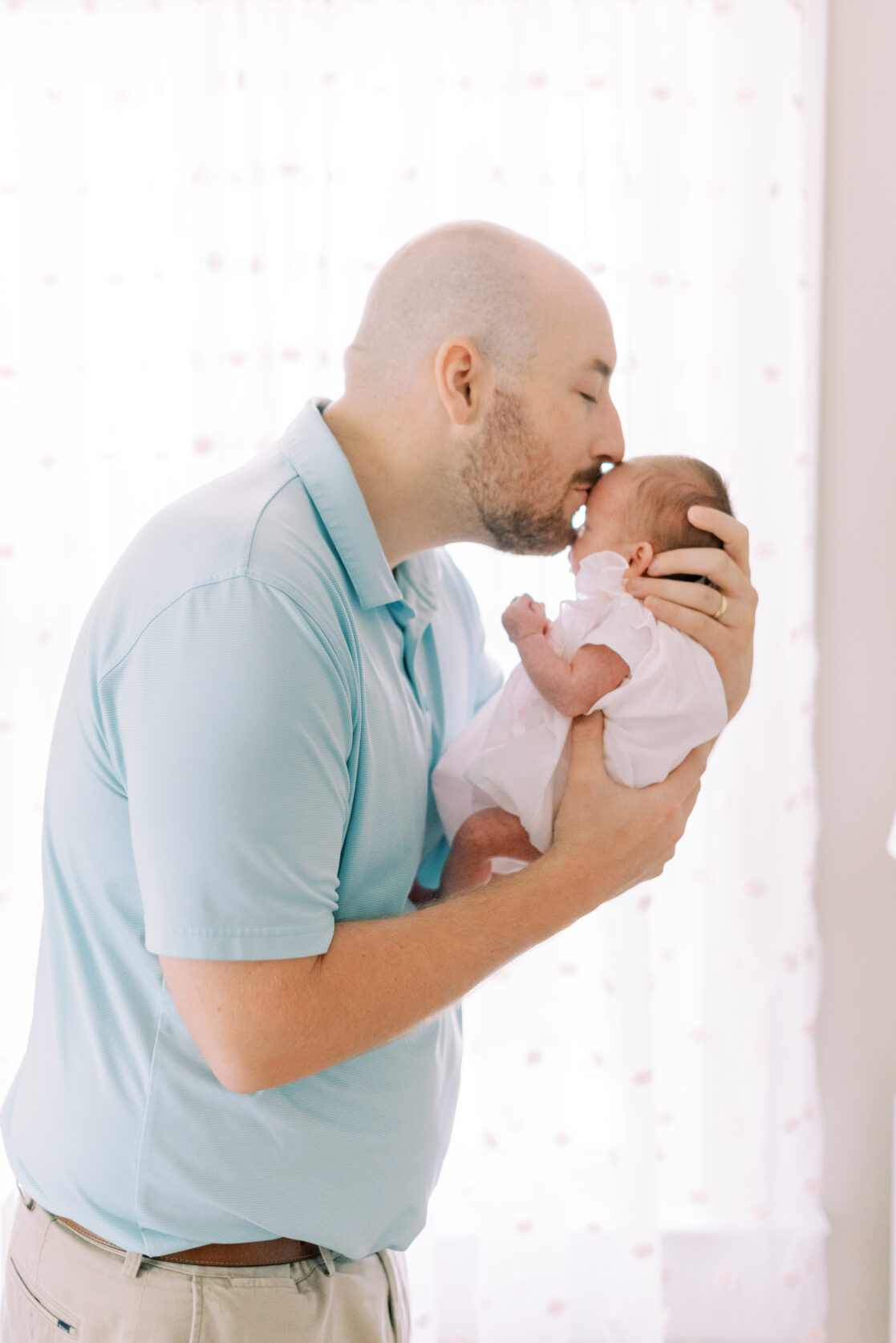 father kissing newborn baby he is holding